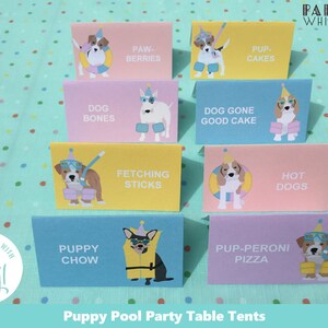 May include: A set of 8 colorful table tent cards featuring illustrations of dogs wearing party hats and swimming gear. The cards have text that says "Puppy Chow", "Paw-Berries", "Pup-Cakes", "Dog Bones", "Fetching Sticks", "Dog Gone Good Cake", "Hot Dogs", and "Pup-Peroni Pizza". The cards are designed for a "Puppy Pool Party" theme.
