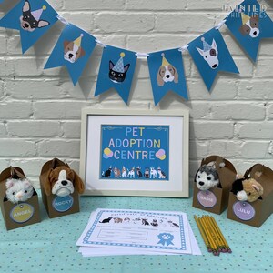 May include: A Pet Adoption Centre party set up with a blue and white banner, a framed sign that says "Pet Adoption Centre", and stuffed animal toys in brown boxes labeled "Angel", "Rocky", "Sadie", and "Lulu".