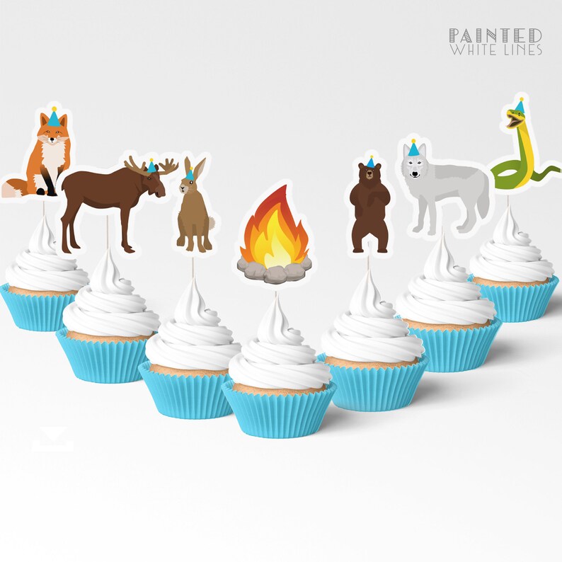 May include: Set of 8 cupcake toppers featuring woodland animals wearing party hats. The animals include a fox, moose, rabbit, bear, wolf, and snake. There is also a campfire topper. The toppers are printed on white cardstock and have a painted white lines design.