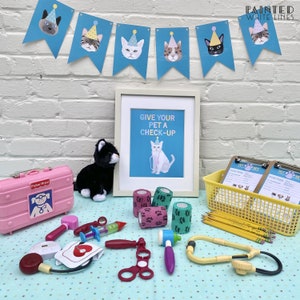 Puede incluir: Una bolsa de m&eacute;dico de juguete rosa, un gato de peluche negro, una impresi&oacute;n enmarcada que dice "Give your pet a check-up", y una cesta amarilla con dos portapapeles que dicen "Pet Vet" y una variedad de suministros m&eacute;dicos de juguete sobre una superficie de lunares azules y blancos.