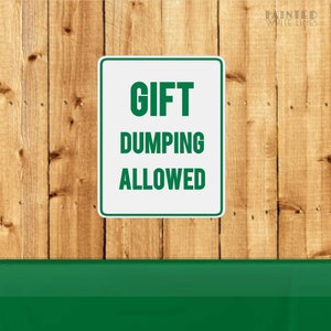 K&ouml;nnte beinhalten: Ein wei&szlig;es Schild mit gr&uuml;nem Text, auf dem "GIFT DUMPING ALLOWED" steht, vor einem Holzgrund.