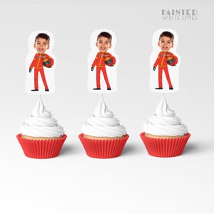 May include: Three red and white cupcake toppers with a photo of a child wearing a red racing suit and holding a helmet. The toppers are on top of red cupcake liners with white frosting.