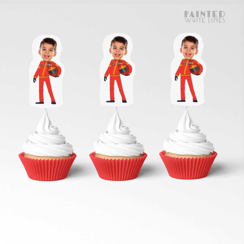 May include: Three red and white cupcake toppers with a photo of a child wearing a red racing suit and holding a helmet. The toppers are on top of red cupcake liners with white frosting.