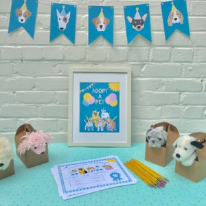 Puede incluir: Un p&oacute;ster enmarcado con el texto "Adopta una mascota" e ilustraciones de perros y globos. Tambi&eacute;n hay juguetes de peluche para perros en bolsas de papel marr&oacute;n, un certificado de adopci&oacute;n y l&aacute;pices sobre una mesa con estampado azul y blanco.