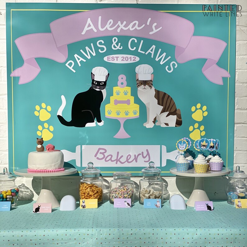 Może przedstawiać: Turkusowo-r&oacute;żowy szyld z napisem "Alexa's Paws & Claws Bakery Est 2012" z ilustracjami dw&oacute;ch kot&oacute;w w czapkach szefa kuchni. St&oacute;ł z tortem, babeczkami i słoikami z przekąskami.