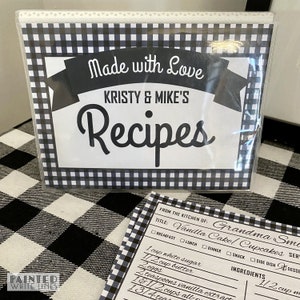 May include: A black and white checkered recipe binder with the text "Made with Love Kristy & Mike's Recipes" on the front. A recipe card is visible with the title "Vanilla Cake/Cupcakes" and a list of ingredients.