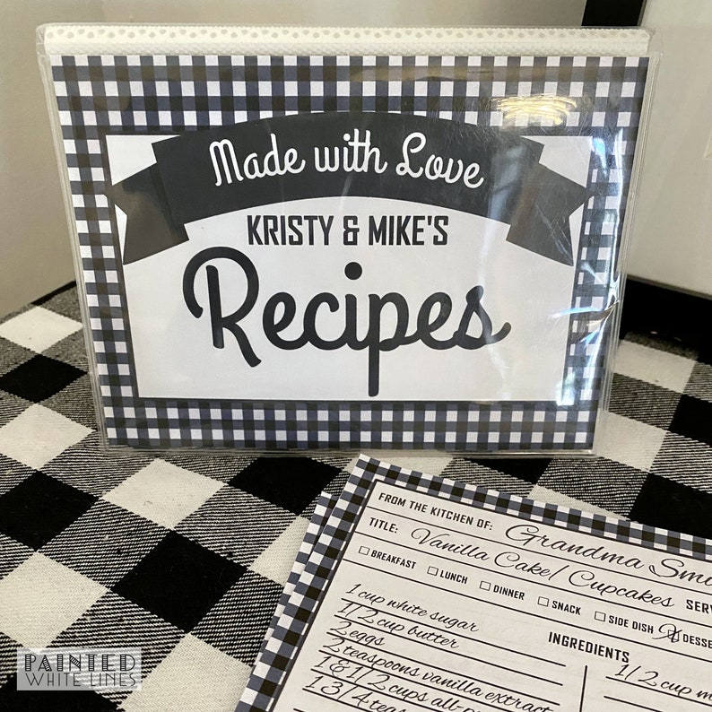 May include: A black and white checkered recipe binder with the text "Made with Love Kristy & Mike's Recipes" on the front. A recipe card is visible with the title "Vanilla Cake/Cupcakes" and a list of ingredients.