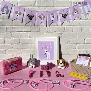 May include: A pink table set up for a pretend pet doctor's office. There are two pink toy stethoscopes, a toy medical kit, a toy hammer, bandages, and two stuffed dogs. A framed sign reads "Give your pet a check-up".