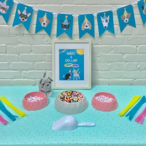 May include: A party-themed craft kit with a blue banner featuring dog faces wearing party hats. The kit includes a framed sign that says "MAKE A COLLAR", three bowls of beads, pipe cleaners, a scoop, and a stuffed dog.