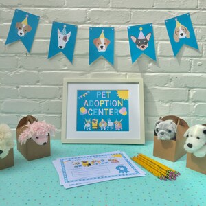 May include: A blue and yellow banner with cartoon dogs on it hangs above a framed sign that says "Pet Adoption Center". There are stuffed animals, a certificate of adoption, and pencils on a blue and white patterned table.
