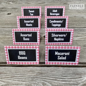 May include: Eight red and white gingham table cards with black text. The cards list various food and beverage options for a party or event. The text on the cards reads: Sweet Tea, Assorted Meats, Assorted Buns, BBQ Beans, Adult Beverages, Condiments/Toppings, Silverware/Napkins, Macaroni Salad.