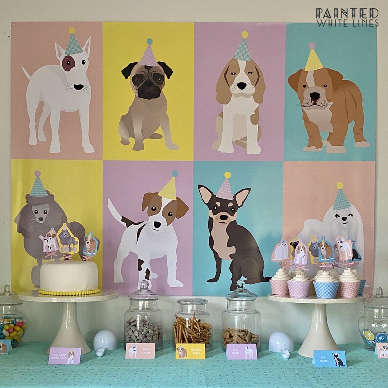 May include: A colorful dog-themed party display featuring a backdrop with illustrated dogs wearing party hats. A cake and cupcakes are decorated with dog toppers. Jars of treats and small signs complete the festive scene.