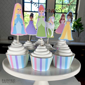 May include: A set of cupcakes decorated with princess-themed toppers. The cupcakes are topped with white frosting and have pastel striped wrappers. The toppers include a unicorn, a princess in a blue dress, a princess in a green dress, a princess in a purple dress, a princess in a pink dress, and a princess in a yellow dress.