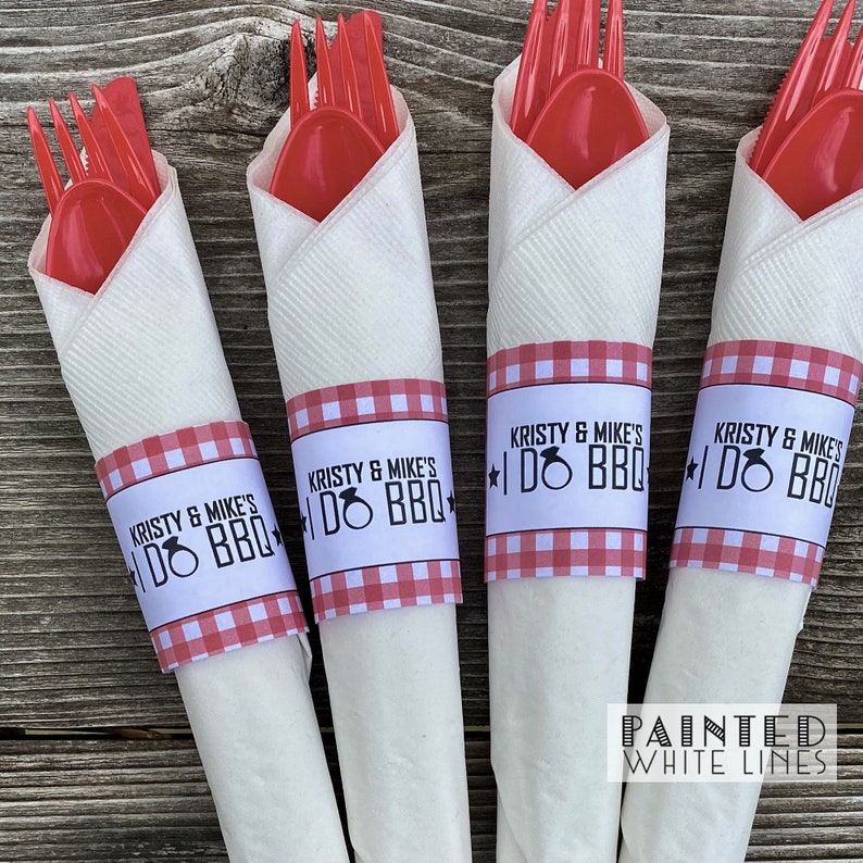 May include: Four white napkins with red and white gingham paper rings. The rings have the text "Kristy & Mike's I Do BBQ" printed on them. The napkins are wrapped around red plastic forks and spoons.