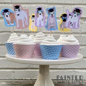 Pode incluir: Seis cupcakes decorados com forros de cupcake com padr&otilde;es azuis e rosa. Cada cupcake tem um cachorro com um chap&eacute;u de formatura e &oacute;culos. Os toppers s&atilde;o impressos com diferentes ra&ccedil;as de c&atilde;es.