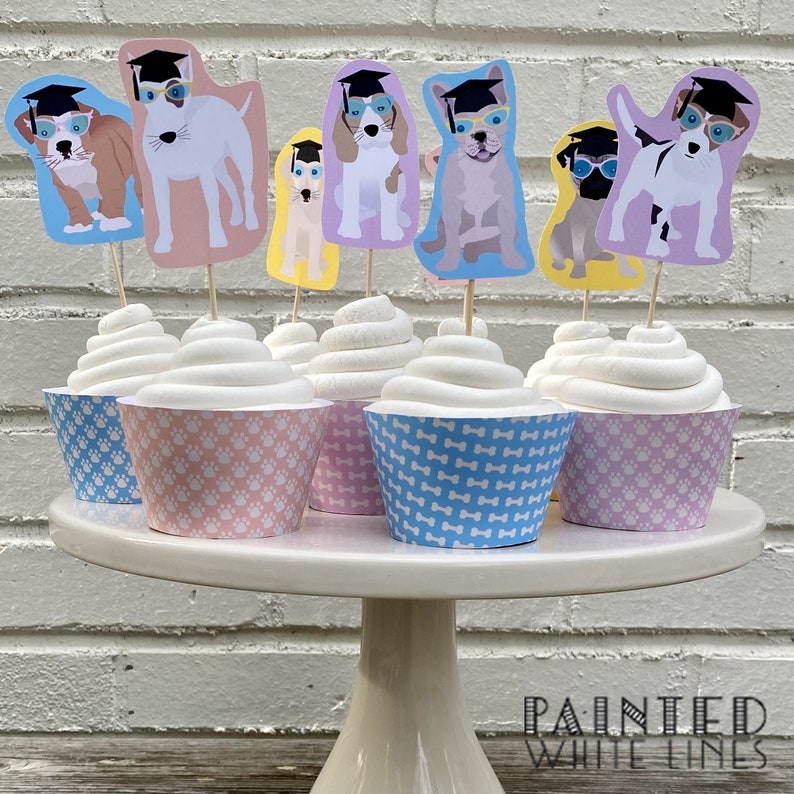 Pode incluir: Seis cupcakes decorados com forros de cupcake com padr&otilde;es azuis e rosa. Cada cupcake tem um cachorro com um chap&eacute;u de formatura e &oacute;culos. Os toppers s&atilde;o impressos com diferentes ra&ccedil;as de c&atilde;es.