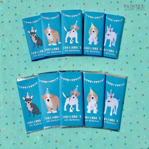 May include: A set of ten chocolate bar wrappers featuring different dog breeds wearing party hats. The wrappers are blue with yellow and white accents and the text "Adrianna's 6th Birthday" is printed on each wrapper.