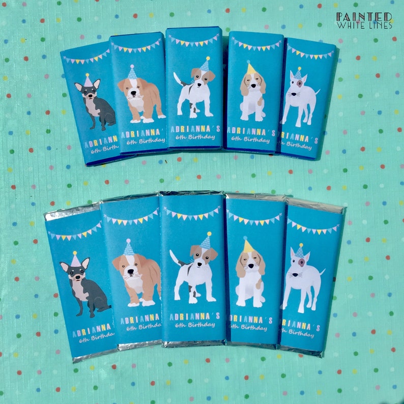 May include: A set of ten chocolate bar wrappers featuring different dog breeds wearing party hats. The wrappers are blue with yellow and white accents and the text "Adrianna's 6th Birthday" is printed on each wrapper.