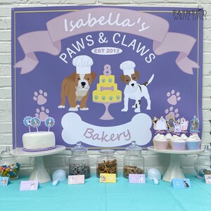 Puede incluir: Un letrero morado y rosa con el texto "Isabella's Paws & Claws Est 2012 Bakery" con un perro de dibujos animados con un gorro de cocinero y sosteniendo un hueso. Hay cupcakes con adornos con tem&aacute;tica de perros en un soporte para pasteles blanco. Hay frascos de golosinas para perros en una mesa con letreros que dicen "Dog Biscuits", "Dog Treats" y "Dog Bones".