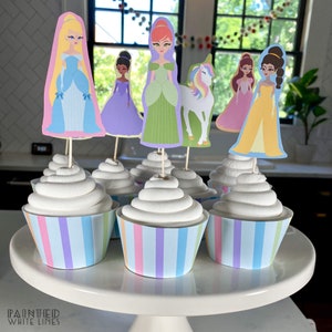 May include: Six cupcakes with pastel-colored striped wrappers and white frosting. Each cupcake is topped with a princess or unicorn character cutout.