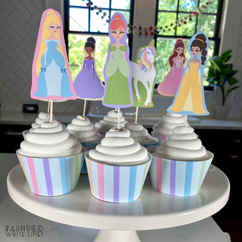 May include: Six cupcakes with pastel-colored striped wrappers and white frosting. Each cupcake is topped with a princess or unicorn character cutout.
