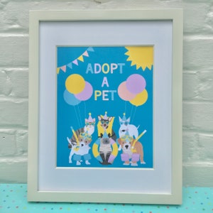 May include: A framed print with a blue background and the text "Adopt a Pet" in white. The print features a group of cartoon animals wearing party hats and sunglasses. There are yellow, pink, and blue balloons in the background.
