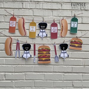 May include: A red, white, and blue birthday banner with a barbecue theme. The banner includes images of hot dogs, hamburgers, grills, ketchup, mustard, and relish. The banner also includes the text "Happy Birthday Kai", "Grill 'n Chill", "Moo Hoodi Kai 21", "Let's Ketchup Dude", "Relish the Day", "Let's Go Kai", and "2".
