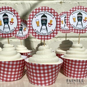 May include: Red and white checkered cupcake liners with white frosting and a round, red and white checkered cupcake topper that says "Barbeque & Brewskis" with a grill, beer, and pacifier graphic. The text "The Smiths" is on the grill. The text "Before Diaper Duties" is below the graphic.