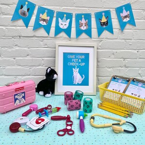 May include: A pink toy doctor's bag, a black plush cat, a framed print that says "Give your pet a check-up", and a variety of toy medical supplies, including a stethoscope, bandages, and a syringe, are arranged on a blue and white polka dot surface.