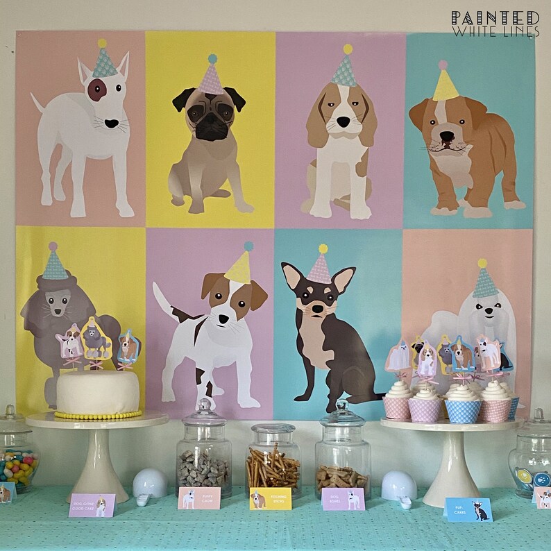 May include: A colourful party backdrop featuring illustrations of dogs wearing party hats. The backdrop is decorated with yellow, pink and blue squares. The table is set with a white cake, cupcakes and jars of treats. The text "Painted White Lines" is at the top of the backdrop.