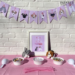 May include: A pink table with a pink tablecloth and three white bowls filled with colorful beads. There are two stuffed dogs on the table, one gray and one brown. A sign on the wall says "Make a Collar".