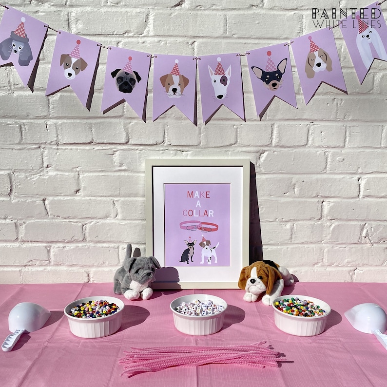 May include: A pink table with a pink tablecloth and three white bowls filled with colorful beads. There are two stuffed dogs on the table, one gray and one brown. A sign on the wall says "Make a Collar".