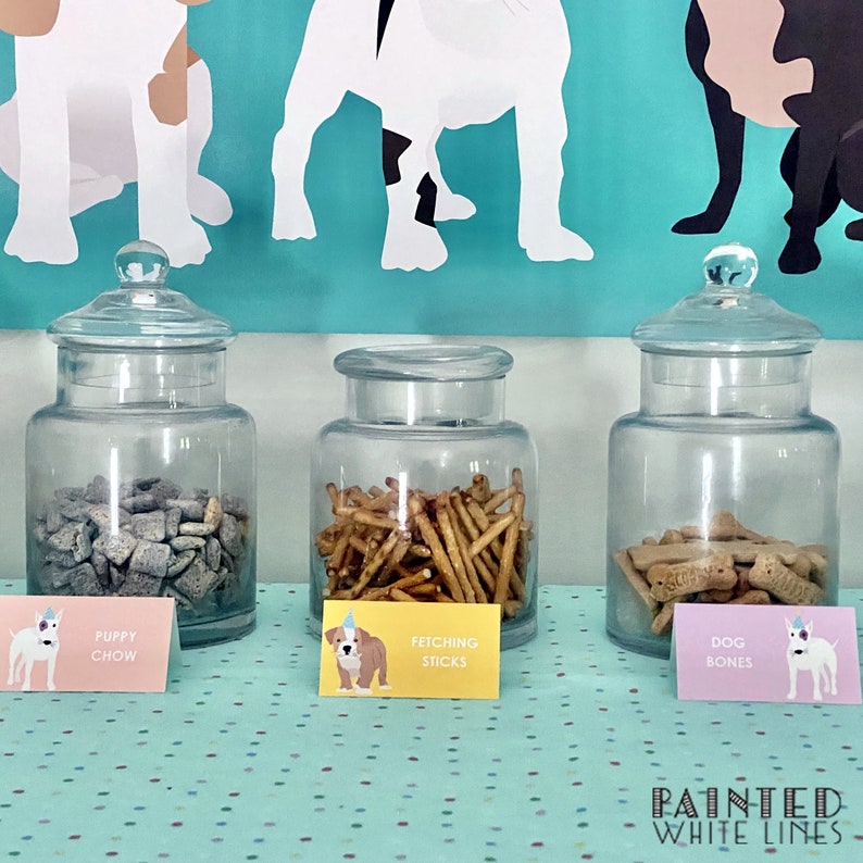 May include: Three glass jars filled with different dog treats. The jars are labeled "Puppy Chow", "Fetching Sticks", and "Dog Bones".