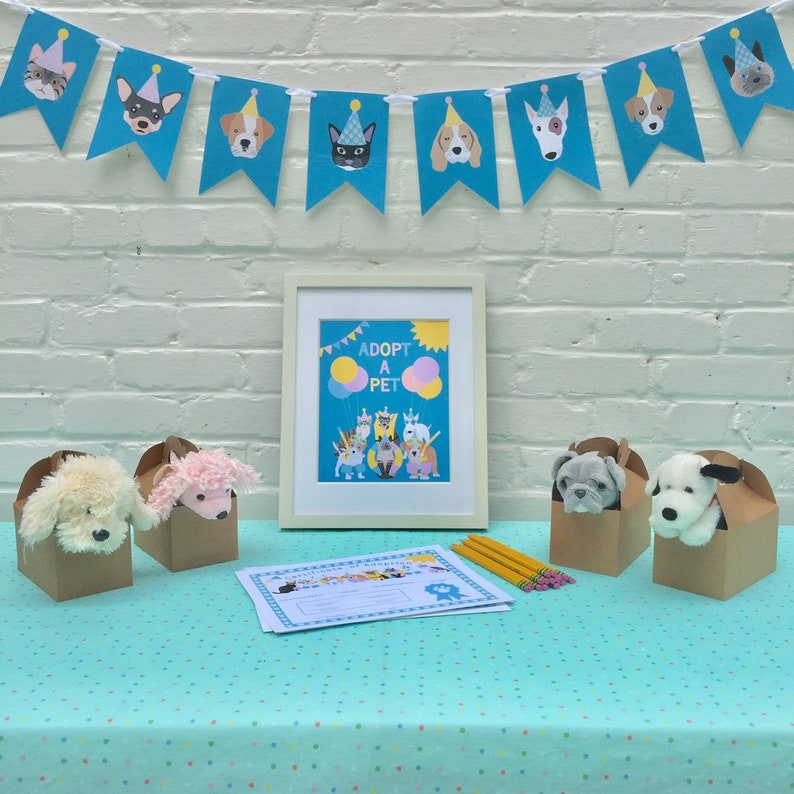 May include: A table covered in a turquoise tablecloth with white polka dots. There are four brown boxes with stuffed animals peeking out of the top. A sign that says "Adopt a Pet" is on the table with a blue and yellow banner behind it.
