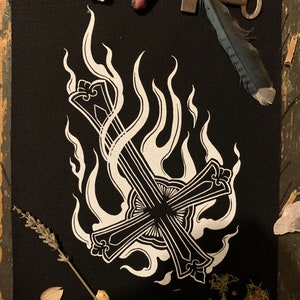 Peut inclure: Un patch noir avec une croix inversée blanche engloutie dans les flammes. Le patch est entouré de divers objets, dont une plume, une clé et une petite pierre.
