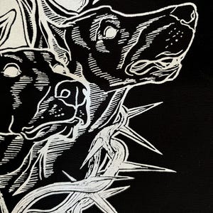 May include: Black and white illustration of a dog's head with a crown of thorns. The dog's head is facing to the right and the crown of thorns is around its neck. The image is in a stylized, graphic style.