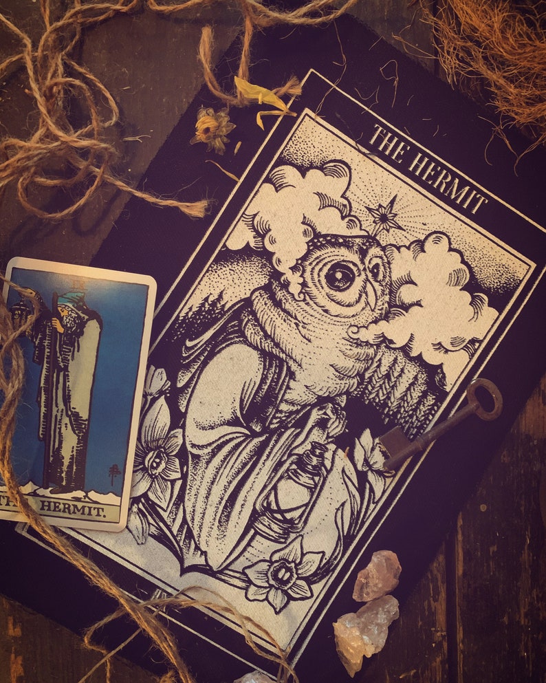 K&ouml;nnte beinhalten: Eine Tarotkarte mit schwarzem Hintergrund und den Worten "The Hermit" in wei&szlig; gedruckt. Die Karte zeigt eine Eule mit einer Laterne in einer dunklen Waldlandschaft.