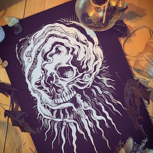 Op de afbeelding: Een zwarte stoffen patch met een wit schedelontwerp. De schedel is omgeven door draaiende lijnen en heeft één oog. De patch is perfect om een ​​gotische touch aan elk project toe te voegen.