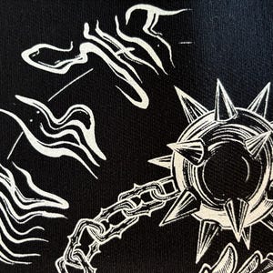 K&ouml;nnte beinhalten: Schwarzer Stoff mit einer wei&szlig;en Illustration einer stacheligen Keule, Ketten und abstrakten Formen. Das Design hat ein mittelalterliches oder Fantasy-Thema mit einem detaillierten, grafischen Stil. Die Keule ist der zentrale Fokus.