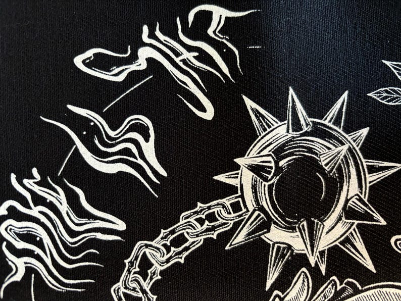 K&ouml;nnte beinhalten: Schwarzer Stoff mit einer wei&szlig;en Illustration einer stacheligen Keule, Ketten und abstrakten Formen. Das Design hat ein mittelalterliches oder Fantasy-Thema mit einem detaillierten, grafischen Stil. Die Keule ist der zentrale Fokus.