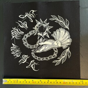K&ouml;nnte beinhalten: Schwarzer quadratischer Aufn&auml;her mit wei&szlig;er Illustration. Das Design zeigt eine Hand, die eine Kette und eine Streitaxt h&auml;lt, umgeben von stilisiertem Text und Bl&auml;ttern. Der Aufn&auml;her misst ca. 10 cm x 10 cm.
