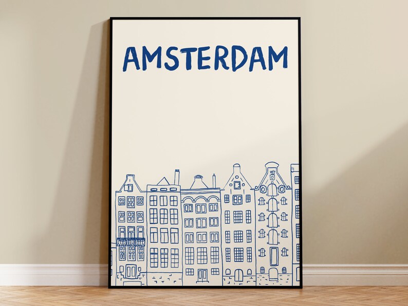 Puede incluir: Una impresi&oacute;n art&iacute;stica enmarcada con la palabra "AMSTERDAM" en azul sobre un dibujo lineal de casas de canal de &Aacute;msterdam. La obra de arte est&aacute; en un marco negro y tiene un fondo color crema.