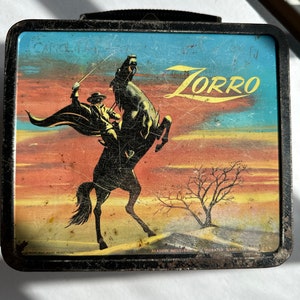 May include: Vintage metal lunchbox featuring a colorful illustration of Zorro on horseback against a sunset backdrop. The lunchbox has the words "Zorro" and "Aladdin Industries" printed on it.