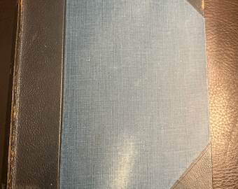 May include: A vintage hardcover book with a blue cloth cover and black leather corners. The book has a worn and aged appearance.