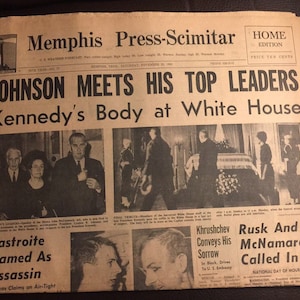 May include: A black and white newspaper front page with the headline "Johnson Meets His Top Leaders" and a subheadline "Kennedy's Body at White House". The newspaper is dated November 23, 1963. The image shows a photo of President Lyndon B. Johnson meeting with other government officials.