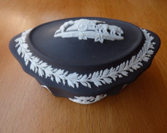 May include: Black and white ceramic trinket box with a raised design of a chariot pulled by two horses. The box is oval shaped and has a white floral border.