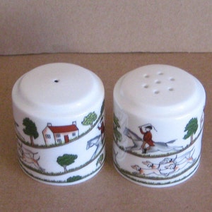 Puede incluir: Un par de saleros y pimenteros de cerámica blanca. Cada salero y pimentero tiene forma cilíndrica con una ilustración detallada de una escena de caza de zorros. Los saleros y pimenteros tienen un acabado brillante y están diseñados para usar en la mesa.