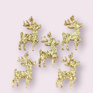 May include: Five gold glitter reindeer figurines. Each reindeer has antlers and is standing on four legs. The figurines are arranged on a light pink background. These decorative reindeer are suitable for holiday crafts and decorations.