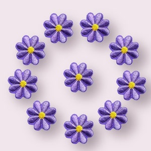 May include: Ten purple felt flower patches with yellow centres. The flowers are arranged in a circle on a white background.