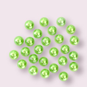 May include: A collection of light green pearl beads scattered on a white surface.